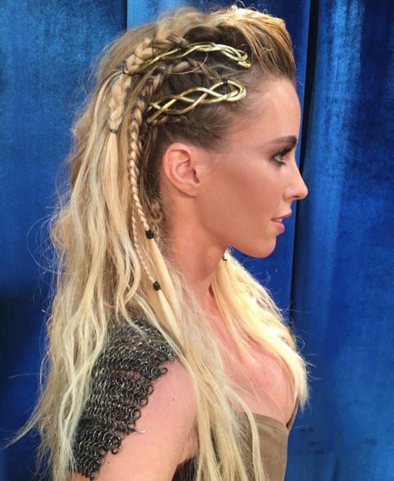 Chica rubia con peinado de vikingos, con trenzas adornadas con broches extravagantes 