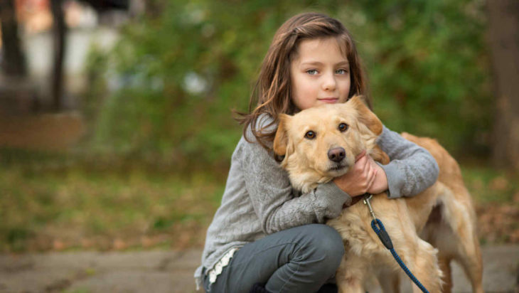 Niña pequeña de ojos verdes abrazando a su perro en un parque