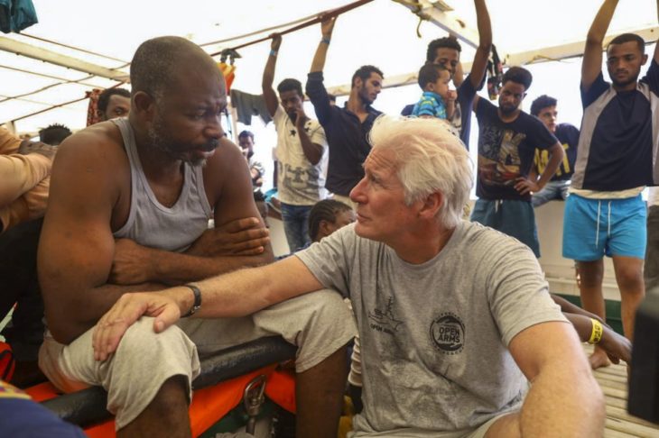 Richard Gere sentado apoya su mano en un migrante rescatado en el Mediterráneo