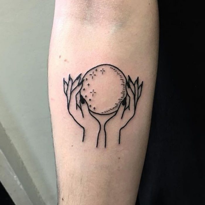 Tatuaje de halloween, manos sosteniendo bola de cristal en estilo minimalista