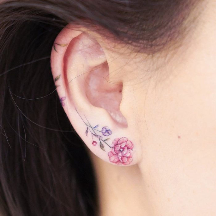 Chica con un tatuaje en la oreja en forma de flores de colores 