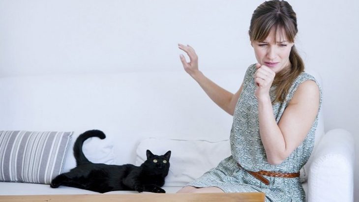 Mujer estornudando porque tiene a un gato negro al lado