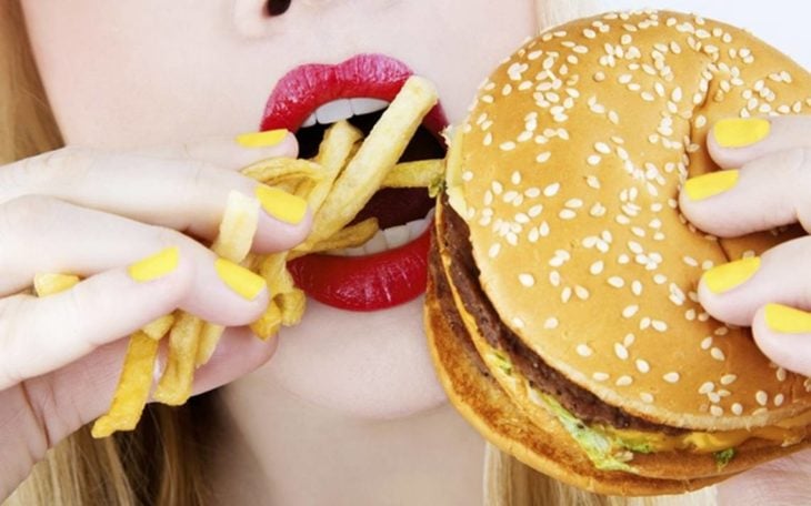 Mujer llevándose a la boca papas fritas y una hamburguesa