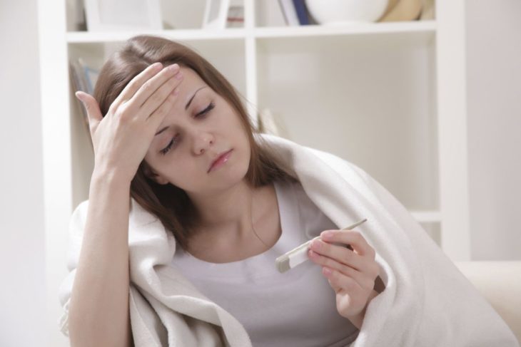 Mujer con fiebre mirando el termómetro