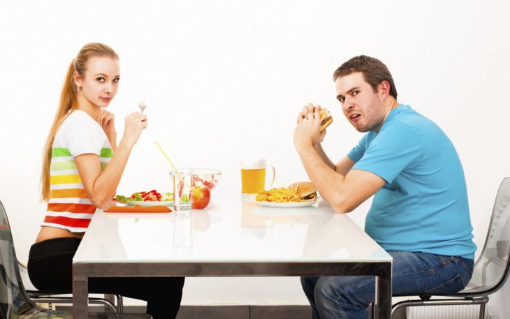 Mujer delgada comiendo saludable y hombre gordito comiendo hamburguesa y papas