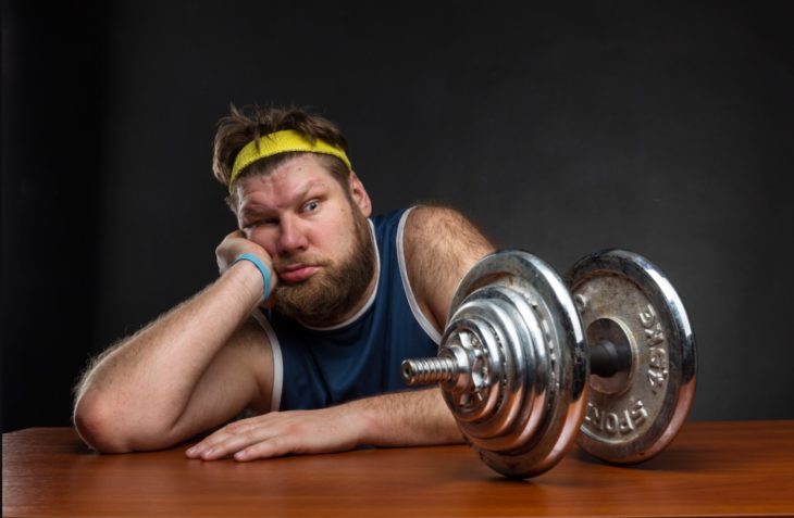 Hombre gordo viendo una pesa de gimnasio