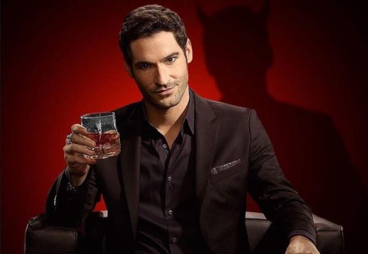 Tom Ellis sosteniendo un whisky en la mano y una silueta del diablo