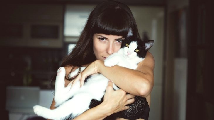 Mujer de cabello negro abrazando a un gato negro y blanco