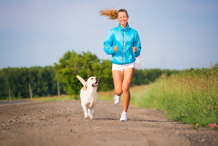 Mujer con ropa deportista corriendo junto a su perro por un campo