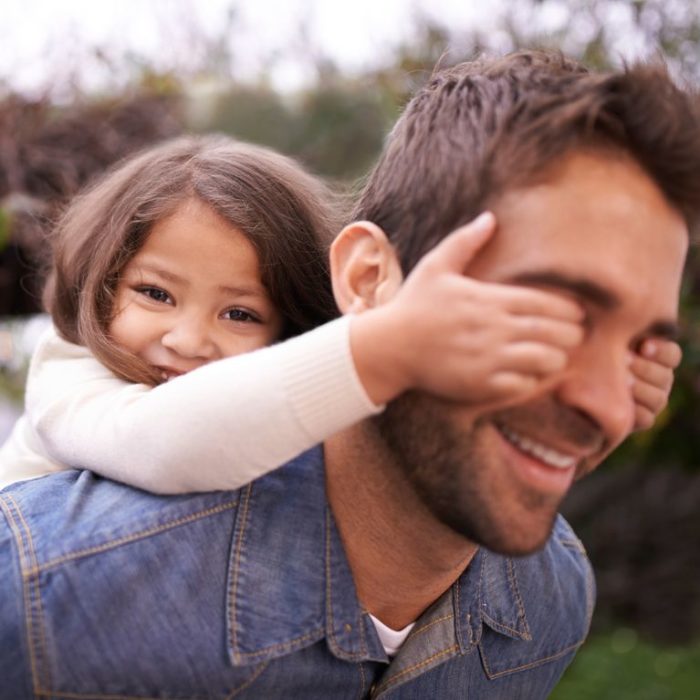 Niña tapándole los ojos a su papá, ambos sonriendo