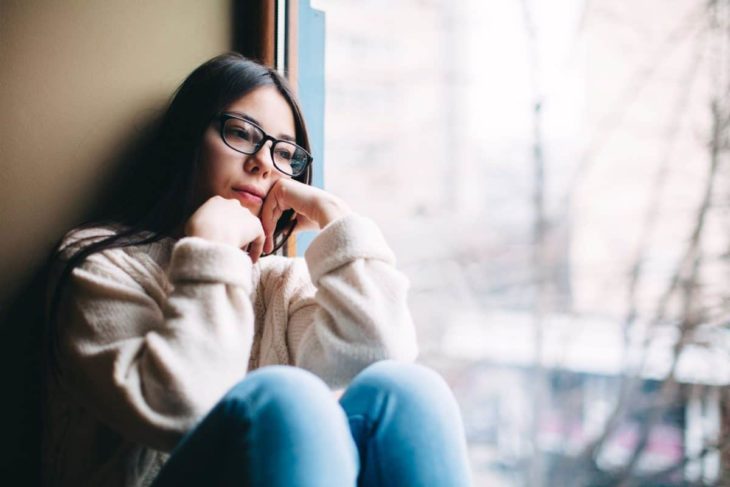 Mujer sentada junto a una ventana pensando