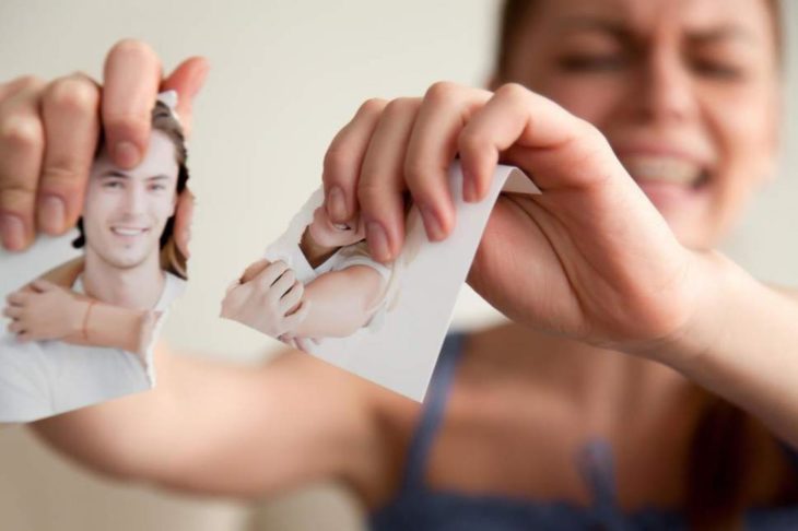 Mujer rompiendo fotografía luego de ruptura amorosa