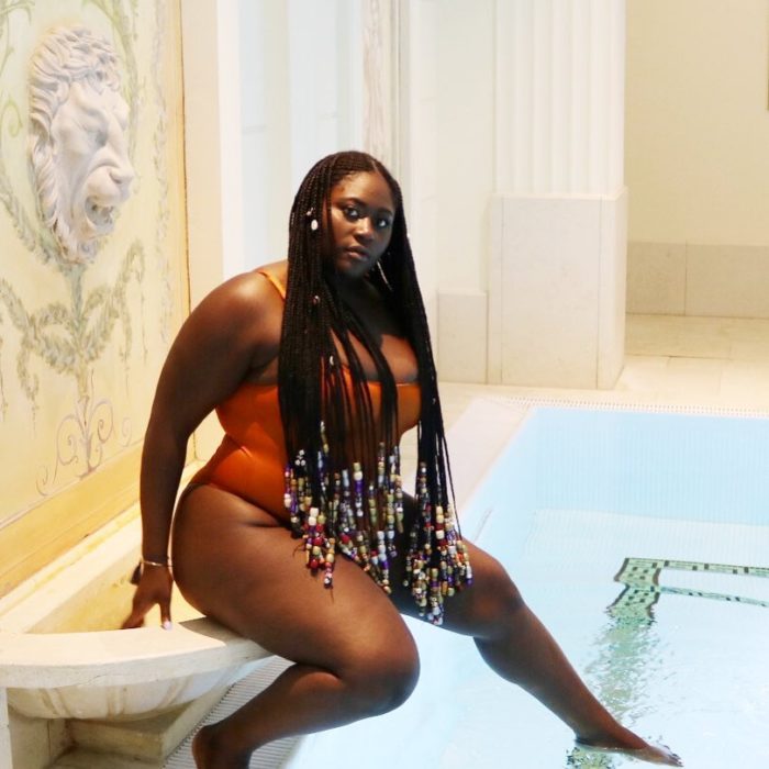 Danielle Brooks sentada a un lado de una alberca con un traje de baño rojo