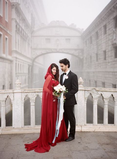 una pareja de novios posa en un puente de un canal, ella con un vestido rojo y una caperuza del mismo color