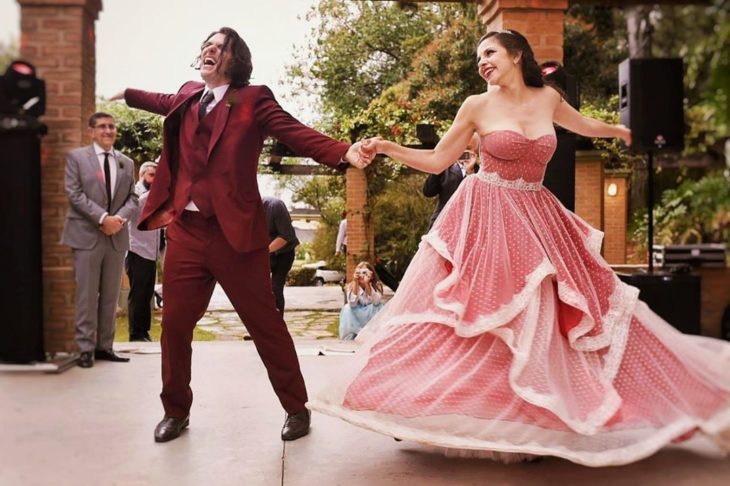 Una pareja de novios baila en una pista, ella con vestido rojo con gasa blanca encima