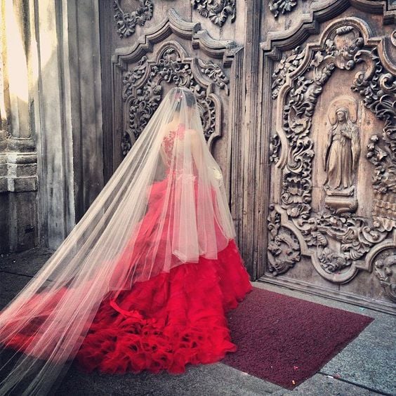 Una novia de vestido rojo y velo blanco a las puertas de un templo