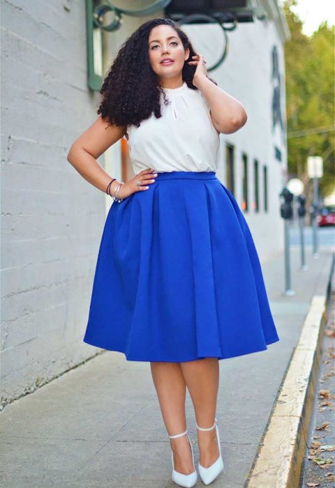 mujer caminando sobre una banqueta vestida con falda azul rey y con blusa blanca