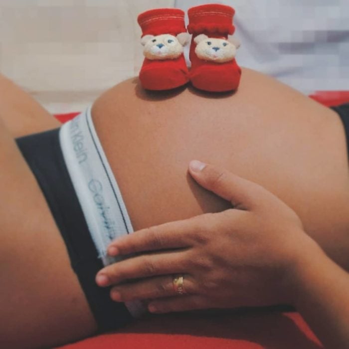 vientre de una mujer embarazada con un par de botitas rojas encima