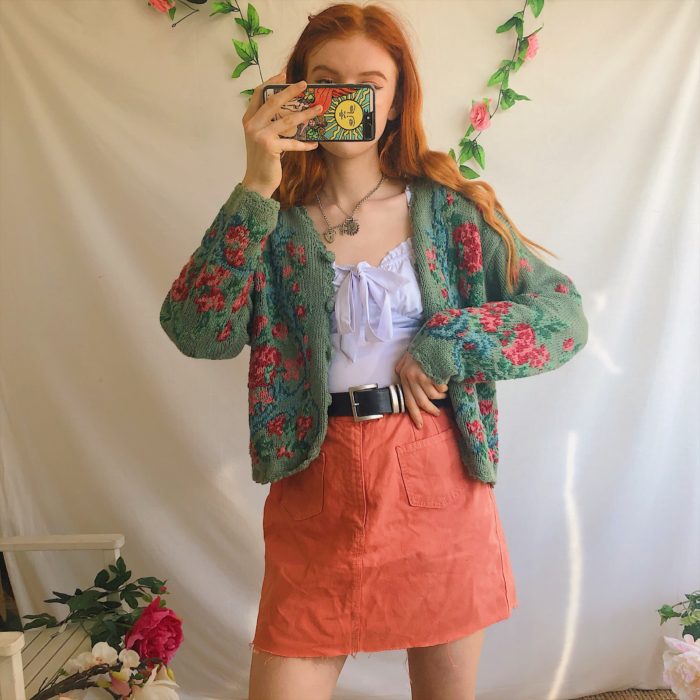 Outfits con cardigans; chica pelirroja con falda color salmón y suéter tejido con botones y flores, estilo abuelita