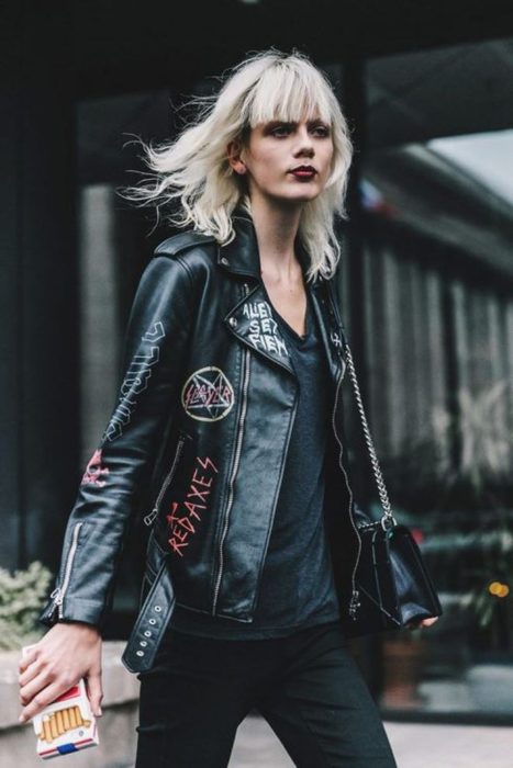 Chica rubia con chaqueta de cuero negra con logos de bandas de rock