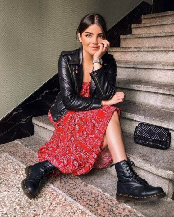 Chica sentada en las escaleras con vestido de tela de paliacate rojo, chamarra de cuero negro, botas Dr. Martens y reloj de mano