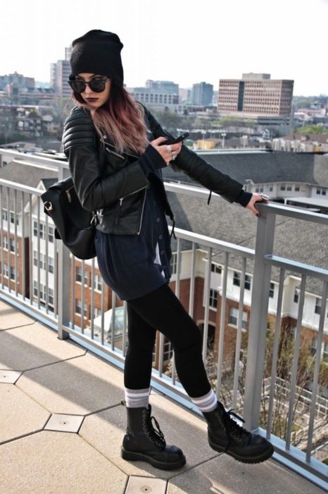 Chica ruda con gorro para el frío, lentes de sol, leggins, botas Dr. Martens con calcetas rayadas y chamarra negra de cuero