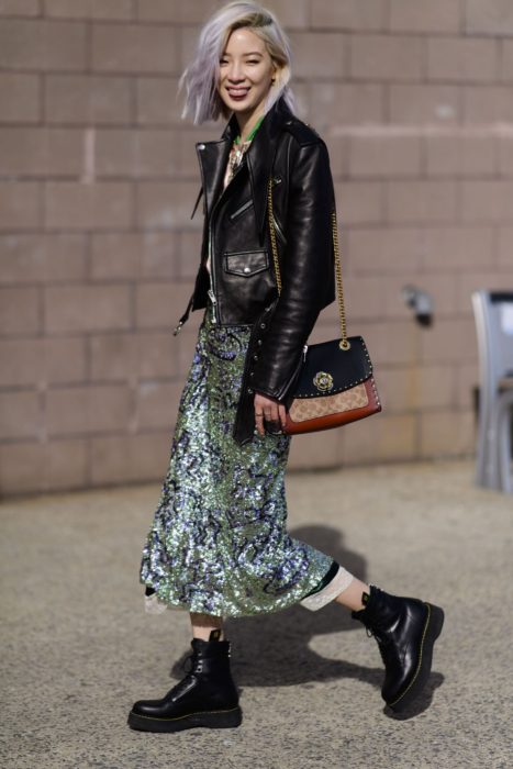 Chica coreana de cabello corto teñido de lila, con chamarra de cuero negro, vestido largo de lentejuelas verdes y botas Dr. Martens