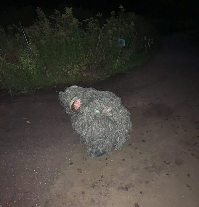 Chica vestida como arbusto en medio de un sendero de un parque 