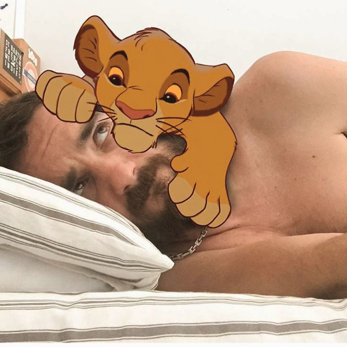 Ilustrador que hace montajes con personajes de Disney recostado en la cama y con Simba bebé sobre su cabeza 