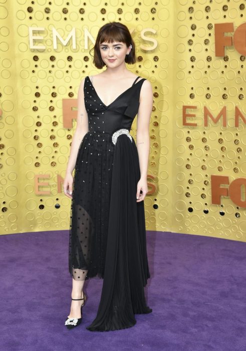 Maisie Williams usando un vestido de color negro con aplicaciones de brillos mientras posa en la alfombra roja de los premios Emmys 2019