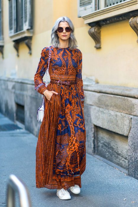 Ropa estilo boho o hippie chic; chica de cabello plateado corto con maxivestido anaranjado y azul con estampado de jirafa, con tenis blancos