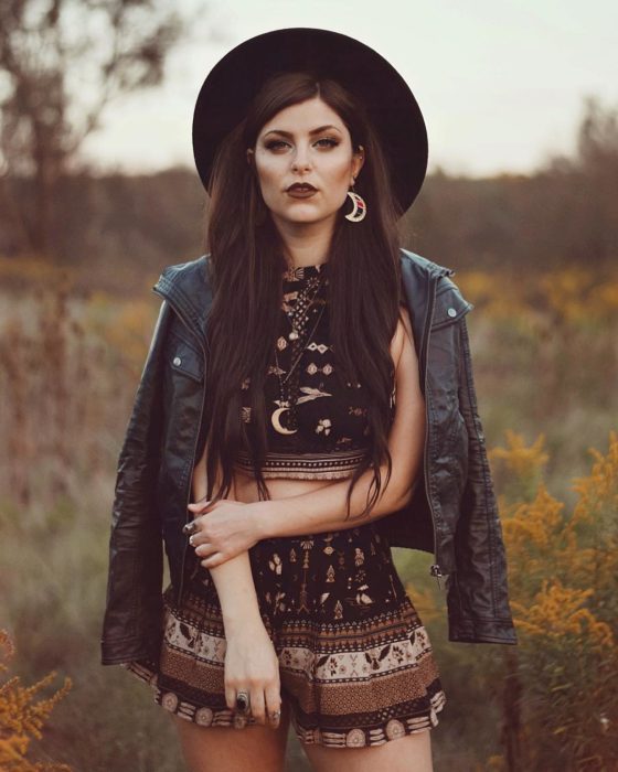 Ropa estilo boho o hippie chic gótica; chica de cabello largo, con aretes de luna, crop top y short de tela de paliacate, chamarra de cuero negro