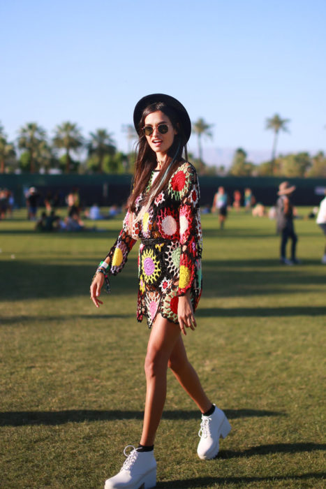 Ropa estilo boho o hippie chic; chica de cabello castaño, lacio y largo, con sombrero, lentes de sol, vestido de flores tejido y tenis blancos de plataforma: mujer en festival de música