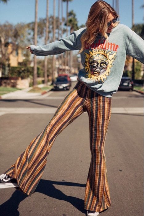 Ropa estilo boho o hippie chic; chica en la calle con pantalón acampanado de rayas verticales con sudadera gris con estampado de sol