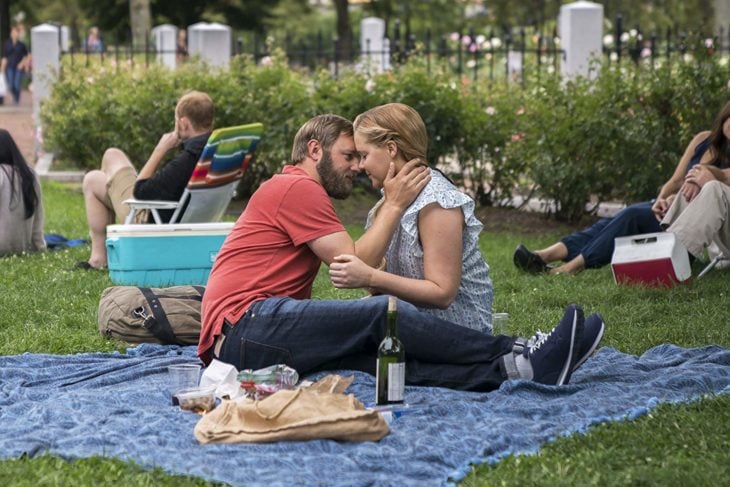 una pareja haciendo un picnic en un parque sentados sobre una manta azul, se tocan la cara
