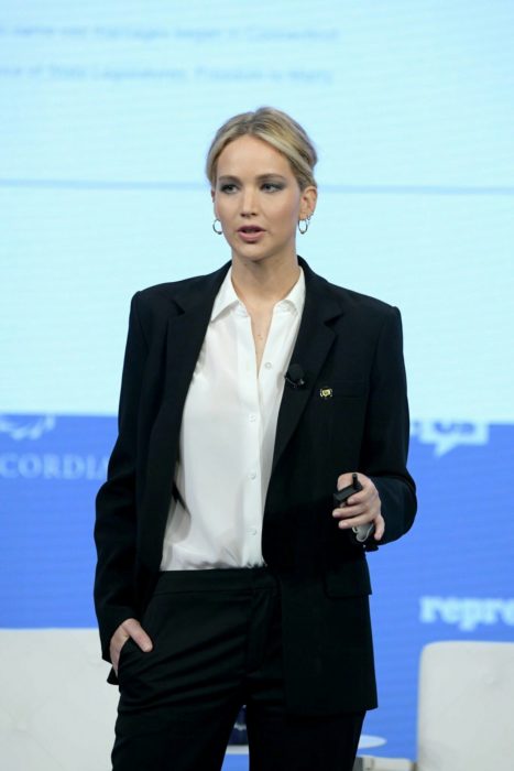 Famosas con traje; Jennifer Lawrence con saco y pantalón de vestir negro con camisa blanca, peinado de cola de caballo sencillo