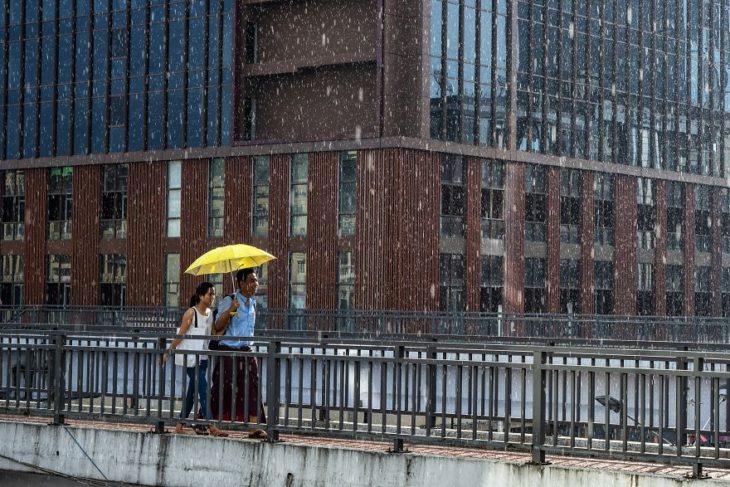 Pareja de novios caminando bajo la lluvia y cubriéndose con una sombrilla 