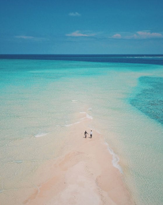 Pareja de novios caminando en medio de una playa que conecta al mar 
