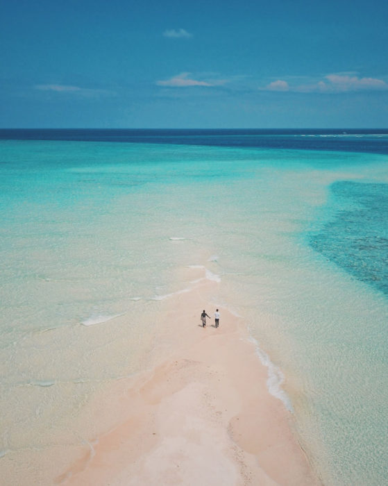 Pareja de novios caminando en medio de una playa que conecta al mar 