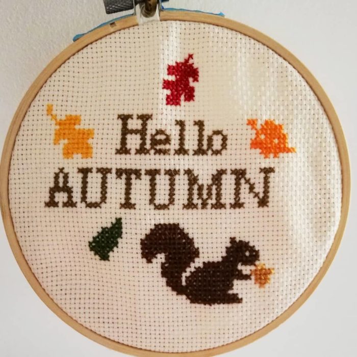 un bastidor y lienzo para bordar punto de cruz con un diseño que dice 'Hello autumn'