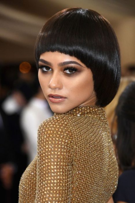 una mujer vestida de dorado de espaldas voltea con un corte bowl en castaño oscuro