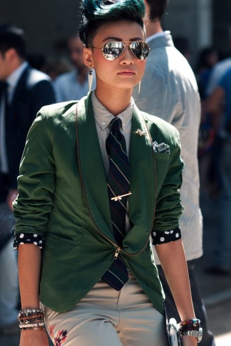 Looks tomboys; mujer con atuendo masculino, saco verde, corbata, pulseras y lentes de sol, con cabello verde con corte mohicano 