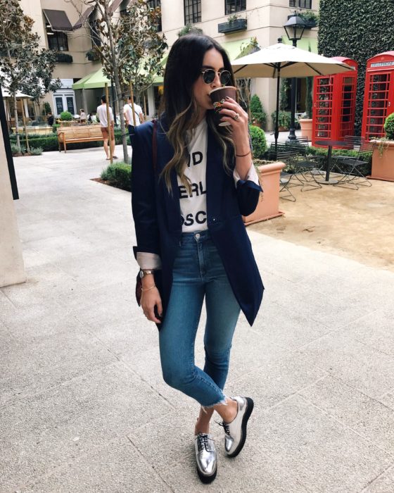 Looks tomboys; chica con atuendo masculino, saco azul marino largo, playera básica blanca, zapatos de plataforma plateados, tomando un café en la calle