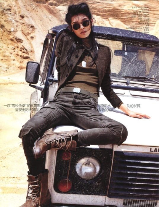 Looks tomboys; chica con atuendo masculino, botas militares, pantalón de mezclilla y saco, sentada en el cofre de una camioneta antigua