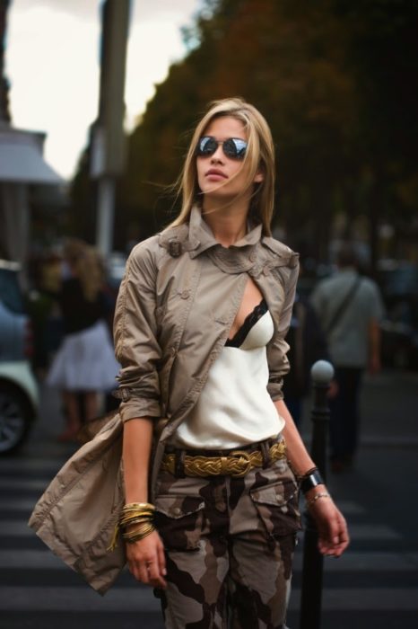 Looks tomboys; mujer con atuendo masculino, pantalón de camuflaje y blusa de seda blanca con encaje y lentes de sol, cruzando la calle