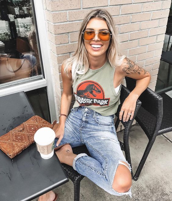 Chica fuera de una cafetería, sentada, sonriendo, llevando outfit con playera de Jurassic Park