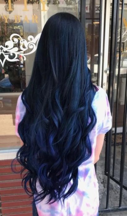 una mujer de espaldas con vestido de colores ycabello que llega hasta las caderas negro con reflejo azul