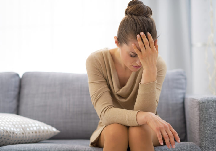 Mujer sentada en el sillón con la mano en la frente como si estuviera pensando mucho