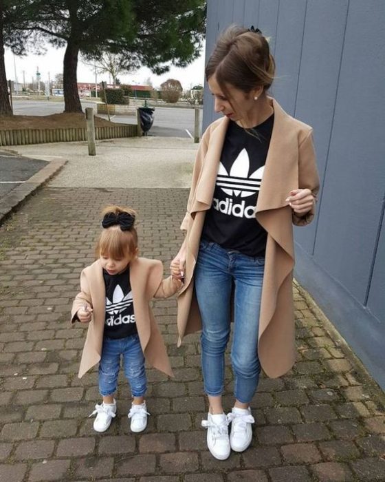 Madre e hija llevando abrigo en tono camel, jeans de mezclilla azul, tenis blancos y blusas negras