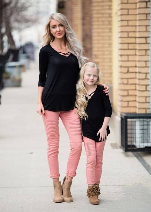 Madre e hija usando outfits iguales con suéteres negros, pantalones rosa palo y zapatos color caqui 